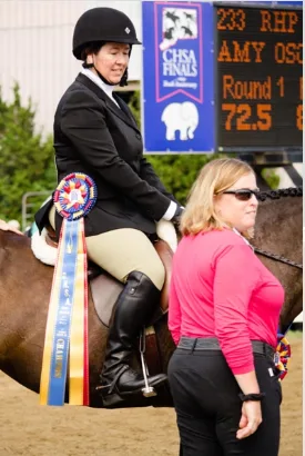 Amy Olszewski on horseback with a tricolor ribbon at CHSA Finals